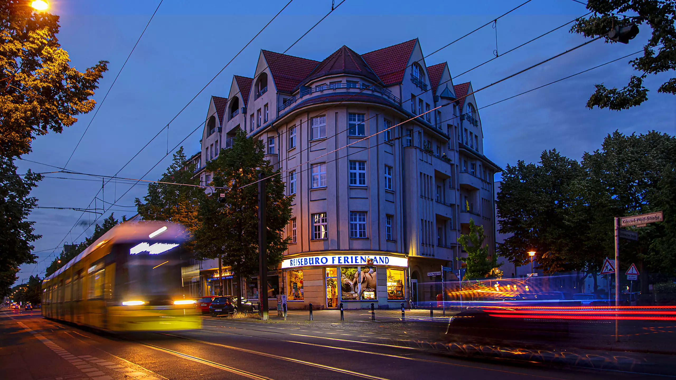 Außenansicht des Reisebüros Ferienland in Berlin am Abend mit Straßenbahn und Straßenszene